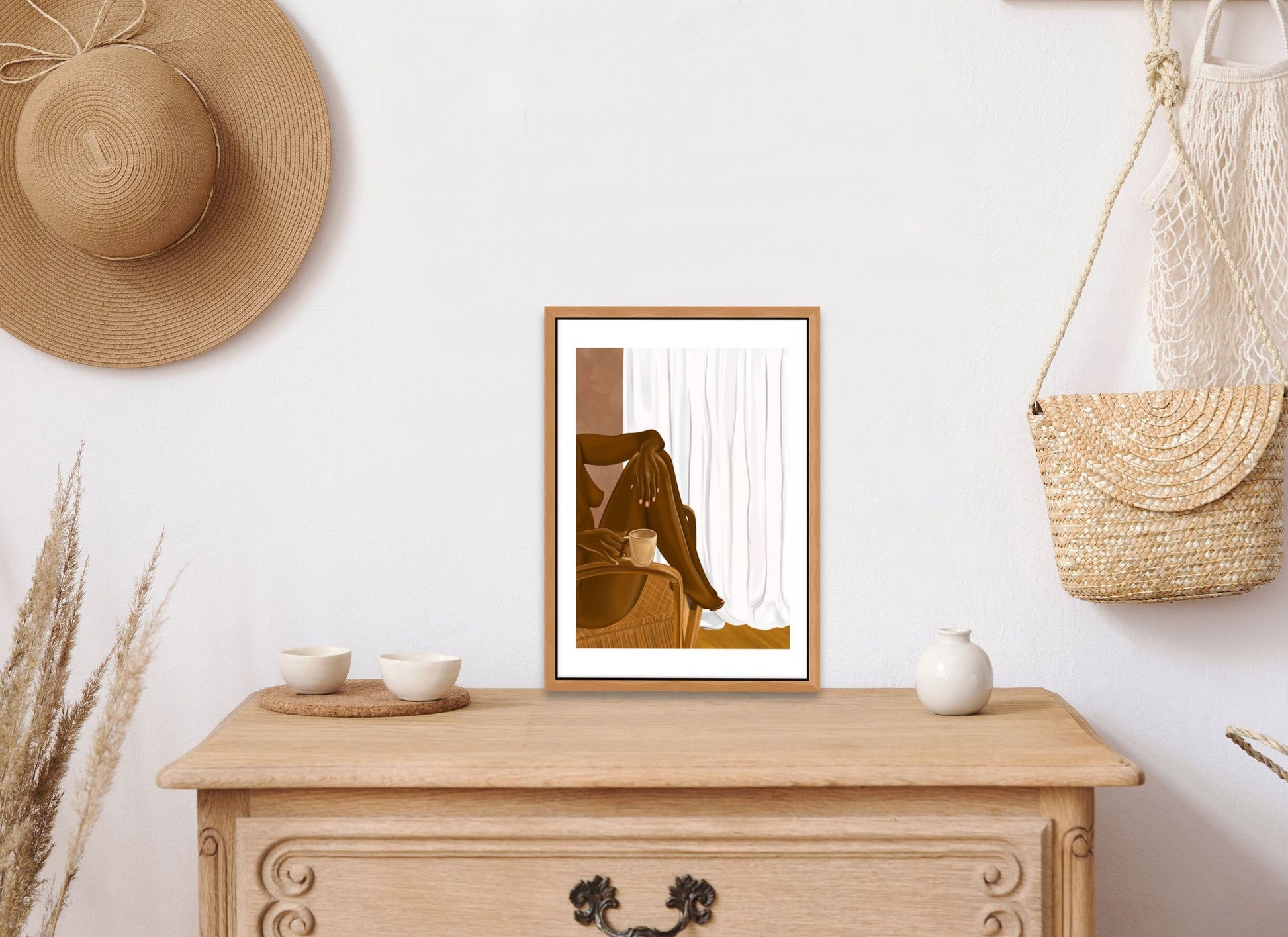 Black artwork print of a nude black woman sitting in a chair framed and resting on top of a chest of drawers in a bedroom