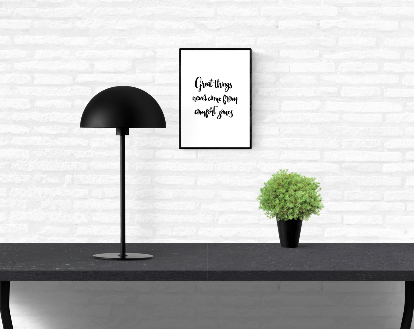 An interior home white brick wall with a mounted motivational quote wall print with the words “great things never come from comfort zones”