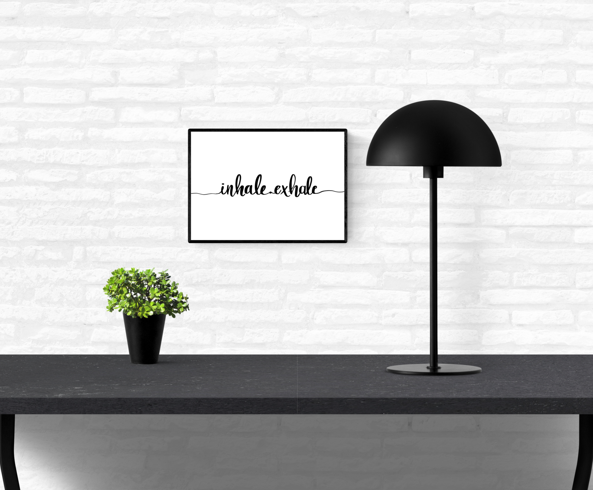 Wall quote print that is framed and mounted on an interior white brick wall with the words, “inhale exhale” written across it