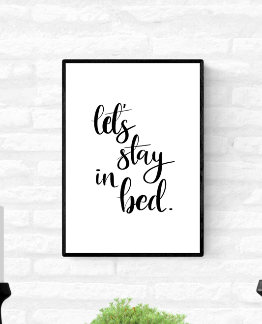 Wall quote print in a thin black frame with the words, “Let’s stay in bed”