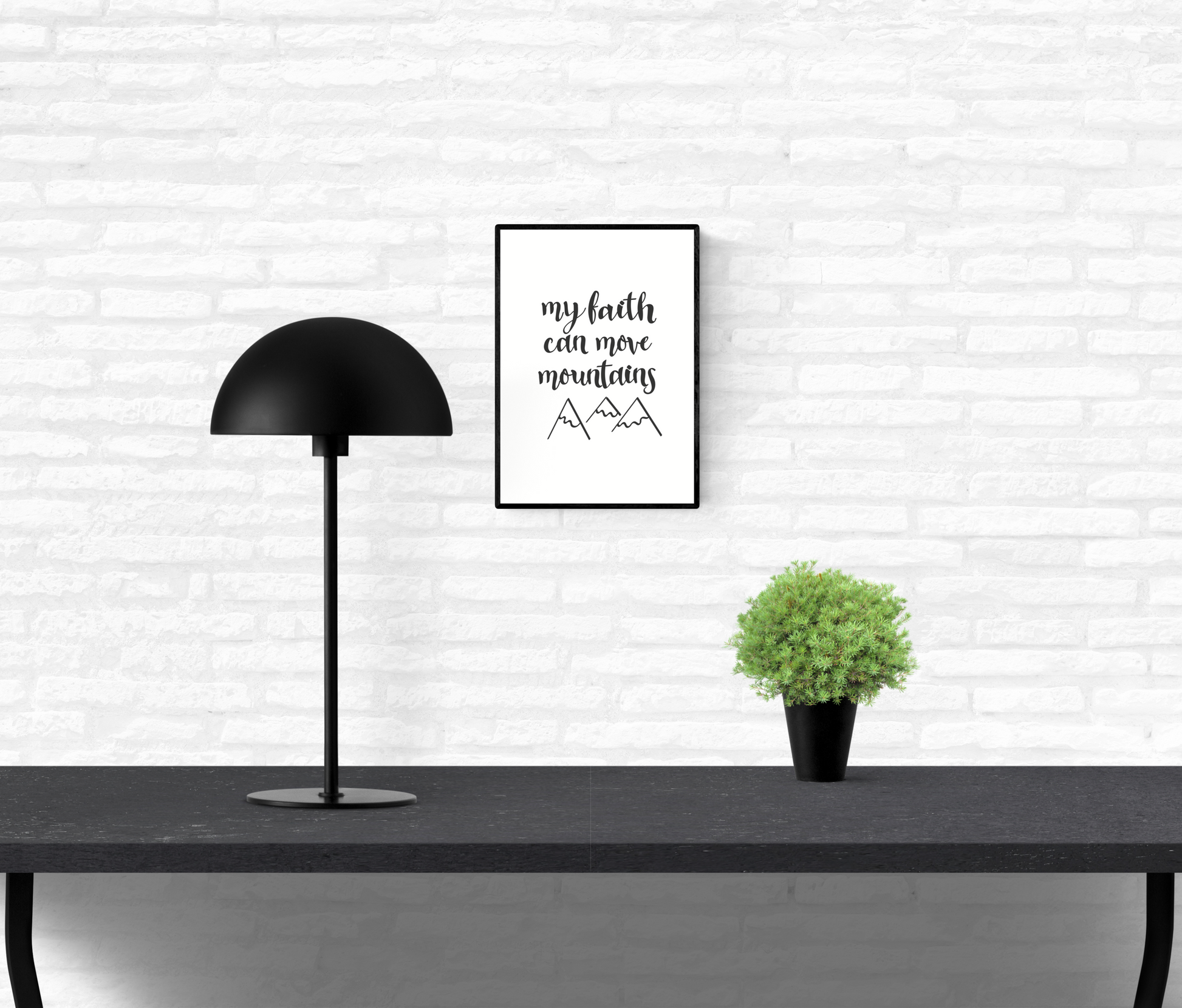 Wall art and quote print with the words, “my faith can move mountains” and line drawings of mountain peaks underneath framed and mounted on an interior white brick wall above a table