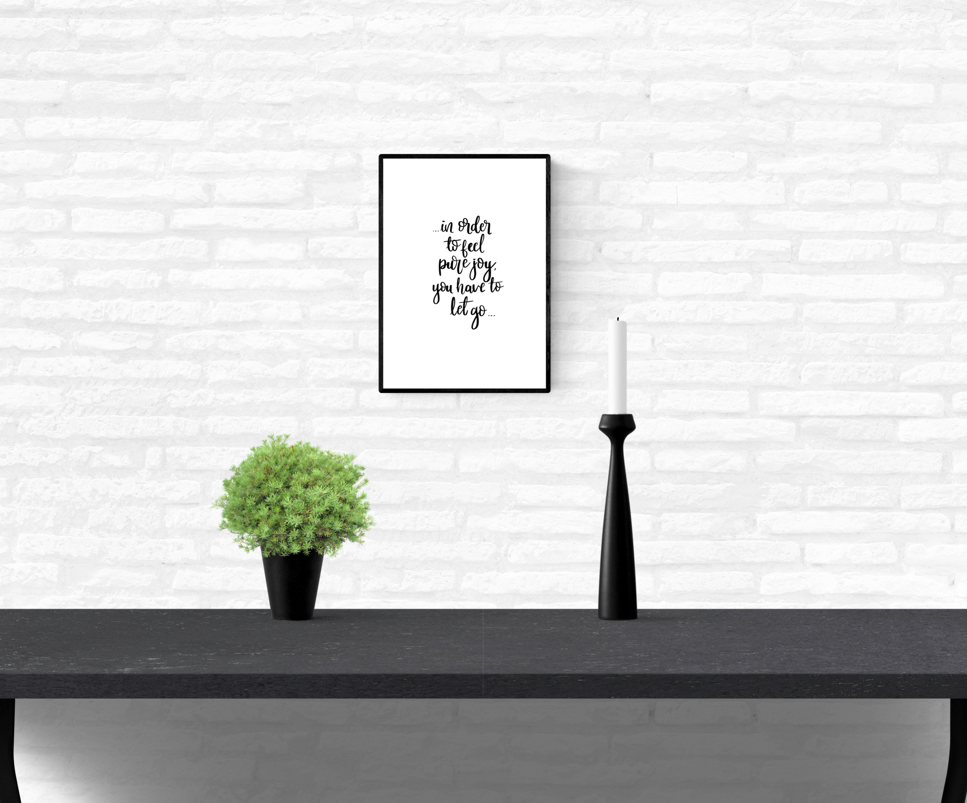 Wall quote print with the words, “in order to feel pure joy you have to let go”, framed and mounted on a home’s interior white brick wall
